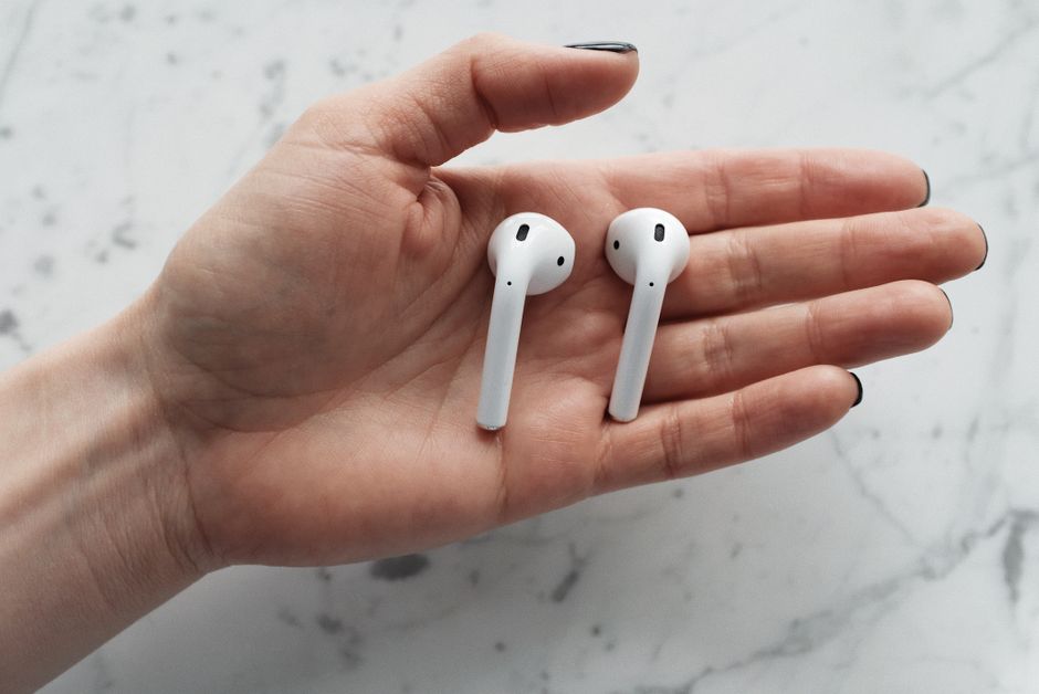 white wireless earbuds close up, person wearing earbuds holding book, apple airpods on desk